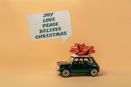 Green car with a red bow on top of it. The words Joy, Love, Peace, Believe are written in a bubble above the carの写真素材