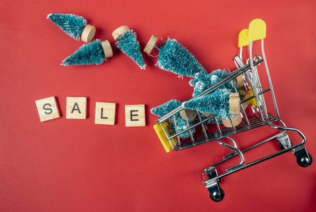 Shopping cart full of Christmas trees with the word Sale written on it. The cart is on a red backgroundの写真素材