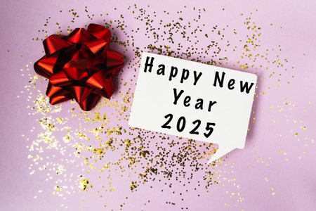 Red bow is on top of a white sign that says Happy New Year 2025. The sign is surrounded by glitter,...