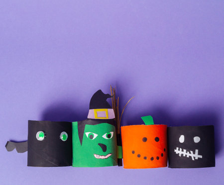 A group of paper Halloween characters are lined up on a purple background. The characters include a witch, a pumpkin, a skeleton, and a ghost. The scene conveys a festive and playful moodの写真素材