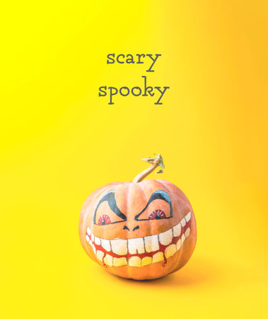 A pumpkin with a scary face painted on it. The pumpkin is sitting on a yellow background.の写真素材