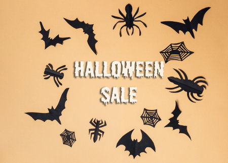 Halloween sale sign with bats and spiders. The sign is on a yellow background. The bats and spiders are in different sizes and shapesの写真素材