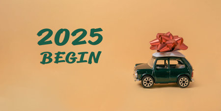 Green toy car with a red bow on top of it. The car is on a yellow background with the words 2025...