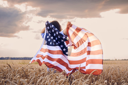 Woman is holding a large American flag in a field. The flag is waving in the wind, and the woman is standing in the middle of the field. Concept of patriotism and freedomの写真素材