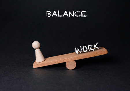 Wooden scale with a person on one side and the word balance on the other. The scale is tilted towards the word workの写真素材