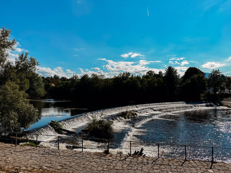 A beautiful blue sky with a few clouds and a river. The water is calm and the trees are lush