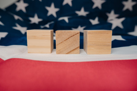 Three wooden blocks are placed on top of a red and white American flag. The flag is the background of the image. The blocks are arranged in a way that they are not touching each otherの写真素材