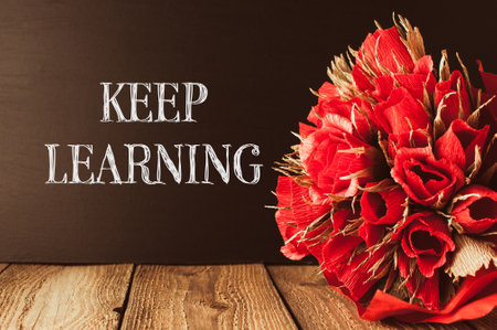A bouquet of red flowers sits on a wooden table with the words keep learning written below it. Concept of growth and progress, as the flowers represent the beauty and potential of learningの写真素材
