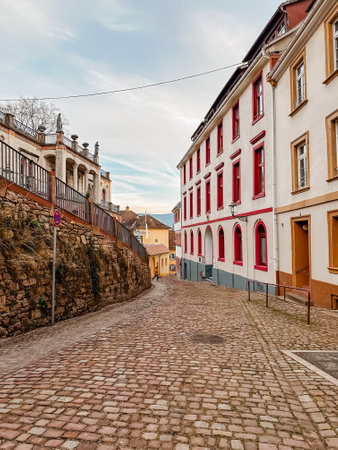 A cobblestone street with a red building in the background. The street is narrow and winding, with a few people walking along it. The atmosphere is quiet and peaceful, with the buildingsの写真素材