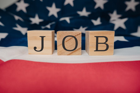 Wooden block with the letters JOB written on it. The block is placed on top of a red and white American flag. The flag is spread out, covering a large portion of the backgroundの写真素材