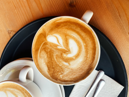 Cup of coffee with a swirl of cream on top sits on a tray. The tray also contains a napkin and a fork. Concept of comfort and relaxation, as coffee is often associated with a warmの写真素材