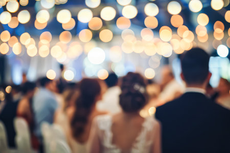 Blurry image of a wedding reception with people sitting in chairs and a bride and groom standing. Scene is celebratory and joyful, as it captures the special moment of a weddingの素材