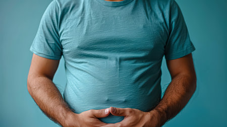 Man with a blue shirt and a stomach full of fat. He is holding his stomach and looking at the cameraの素材