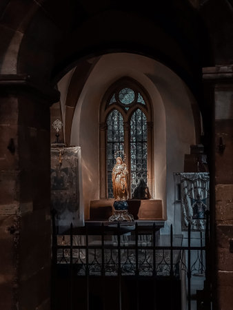Statue of a woman is sitting in a window of a church. The window is stained glass and the statue is surrounded by a small table. The scene is peaceful and sereneの写真素材