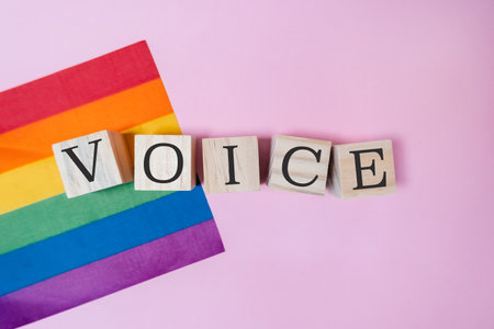 Rainbow flag is on a pink background with the word VOICE written in wooden blocks. The blocks spell out the word in a creative and playful way. Concept of inclusion and empowermentの写真素材
