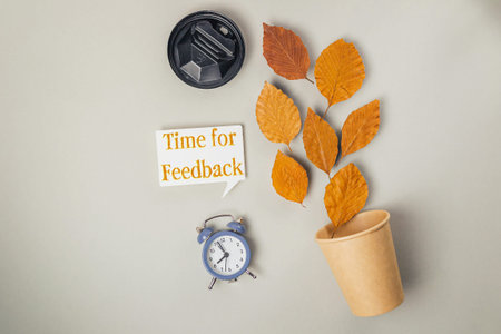 Clock and a cup with leaves on top of it. The leaves are orange and the clock is blue. The words...