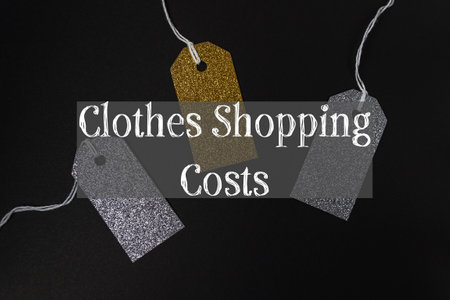Three tags with the word clothes are hanging from a string. The tags are gold and silver. The tags are hanging from a string and are labeled clothes shopping costsの写真素材