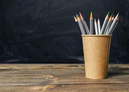 Wooden table with a brown cup of pencils on it. The pencils are of different colors and sizesの写真素材