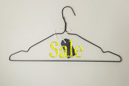Clothes hanger with the word Sale written on it. The hanger is hanging on a wallの写真素材