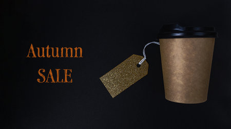 Coffee cup with a tag on it that says Autumn Sale. The tag is gold and is hanging from the cup