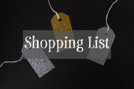 Three tags with gold and silver glitter are hanging from a string. The tags say shopping list