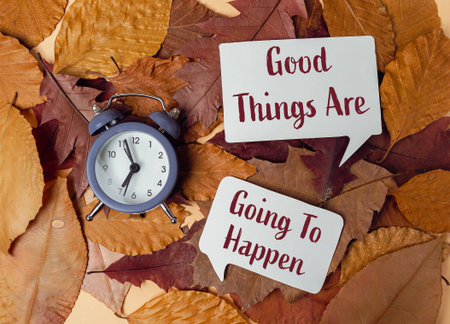 Clock is on the ground with leaves on top of it. There is a white sign that says Good things are going to happenの写真素材