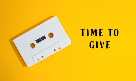White cassette tape with the words time to give written on it. The tape is on a yellow background