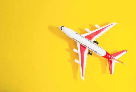 Small red and white airplane is sitting on a yellow background. The airplane is positioned in the middle of the image, and it is a toy or a model. The yellow background adds a sense of warmthの写真素材
