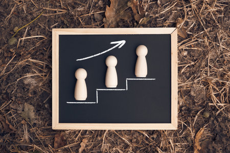 Three wooden figures on a board with a line going up. Concept of climbing the career ladder