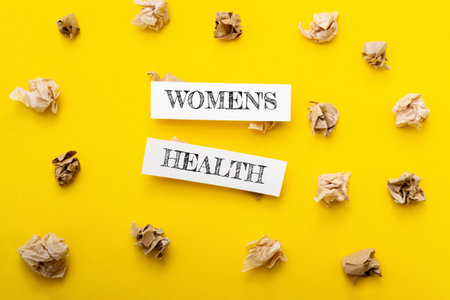 Yellow background with two pieces of paper that say Womens Health on them. The paper is crumpled and scattered around the background, giving the impression of a messy or disorganized environmentの写真素材