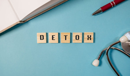 Detox concept displayed with wooden letter tiles spelling detox on a vibrant blue background, accompanied by a pen and stethoscope, creating a health and wellness theme for lifestyle imageryの写真素材