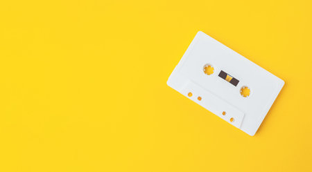 Retro audio cassette positioned on vibrant yellow surface, providing ample copy space for creative...