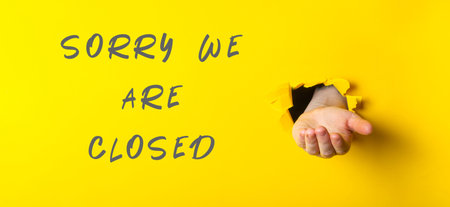 Sorry we are closed sign with a hand holding a hole in it. The sign is yellow and whiteの写真素材