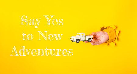Hand holding a toy truck with the words Say Yes to New Adventures written below it. The image is...