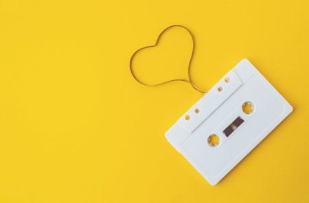 White cassette tape with a heart drawn around it. The tape is laying on a yellow backgroundの写真素材