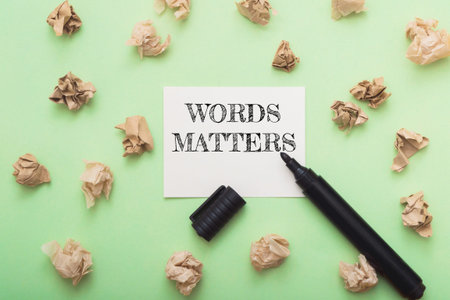 Artistic workspace featuring a note that reads Words Matter with crumpled paper scattered around,...