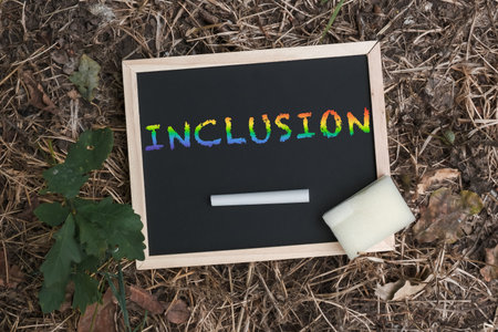 Chalkboard with the word inclusion written on it. The chalkboard is on the ground next to a white...