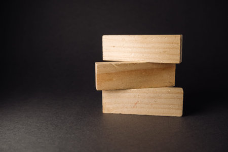 Three wooden blocks are stacked on a dark surface, highlighting their natural grain and texture,...