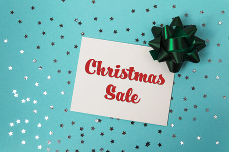 Festive holiday sale announcement card featuring bold red text, adorned with a decorative green bow,...