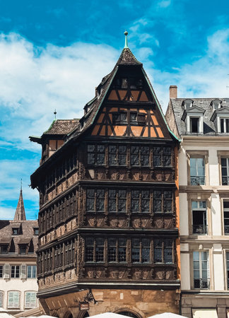Historic timber-framed structure features intricate designs and vibrant colors, surrounded by modern buildings under a bright blue sky, highlighting architectural beautyの写真素材