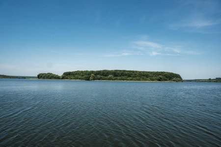 Serene landscape showcases a lush green island nestled in tranquil blue water, with a clear sky...