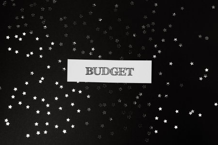 Budget planning concept features a white card with 'BUDGET' text, surrounded by silver star-shaped confetti on a dark background, representing financial aspirations and goalsの写真素材