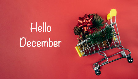 A shopping cart brimming with holiday decorations, including pine cones and a red bow, placed on a...