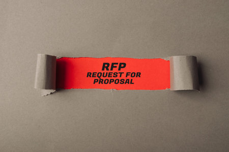 Orange paper strip displays bold black text reading RFP, request for proposal, on a gray surface,...