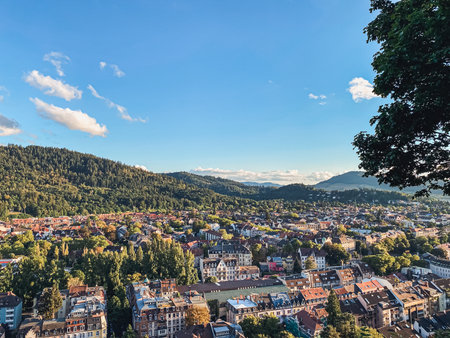 Panoramic cityscape featuring colorful buildings surrounded by verdant hills and a bright sky, illustrating the beauty of urban life in nature with copy spaceの写真素材