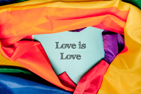 Heart-shaped note with the phrase Love is Love surrounded by colorful fabric, representing...