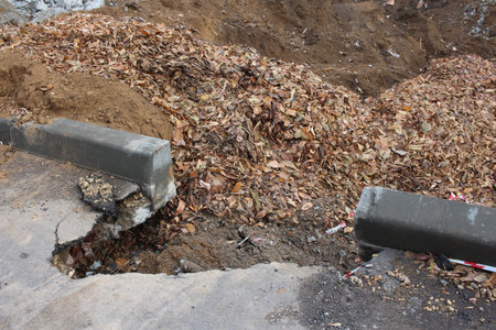 broken curb on the street with a pit destroyed littered with garbage dangerous hole in the asphalt