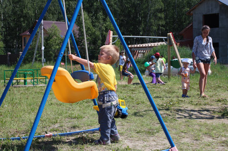 Russia, Novosibirsk, 12.06.2015: a small child boy plays on the playground in the park in the summer on a swingのeditorial素材