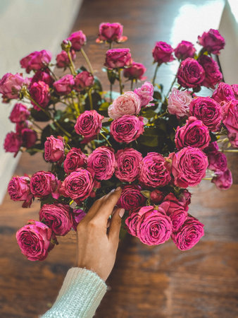 Bouquet of pink roses with a female hand touching flowers on a wooden table, soft natural light and romantic atmosphere.