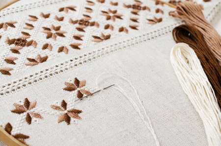 The wooden hoop with the embroidery pattern of brown and beige color on canvas; on wooden table.の写真素材